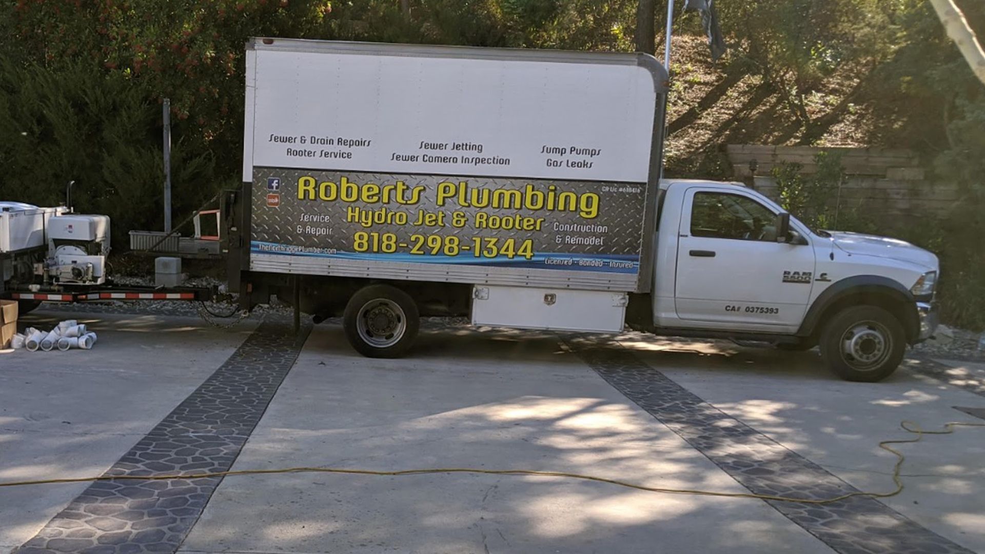 White Roberts Plumbing truck parked on a patterned concrete surface with plumbing supplies nearby.