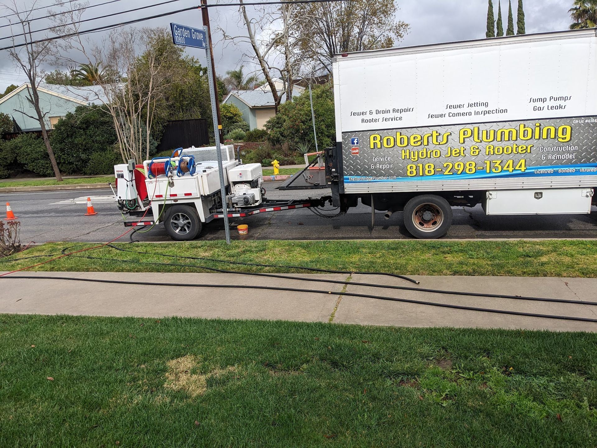 A Roberts Plumbing truck with trailer parked on a street near a sidewalk and houses.