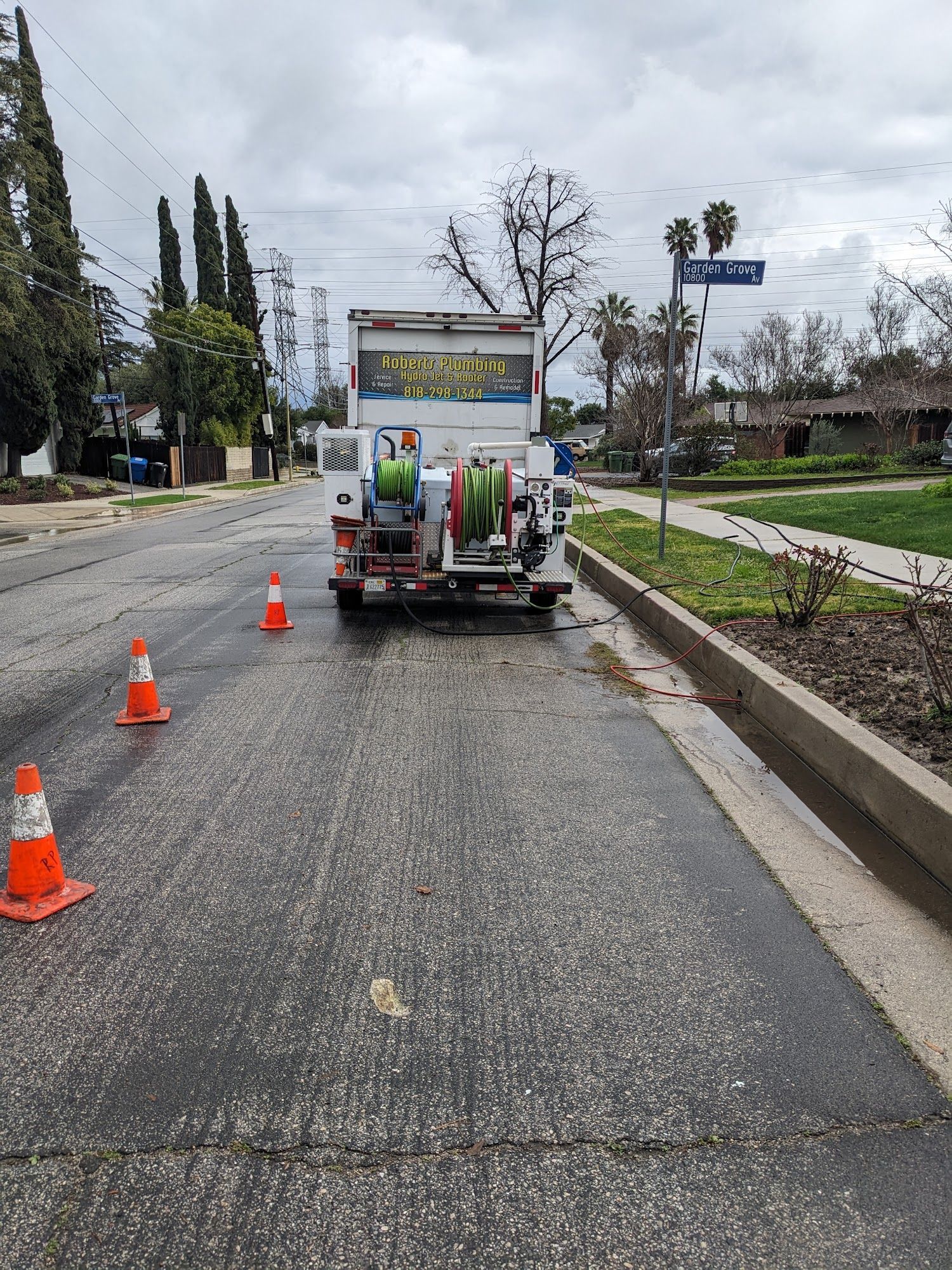A truck with open back on a wet street surrounded by cones.
