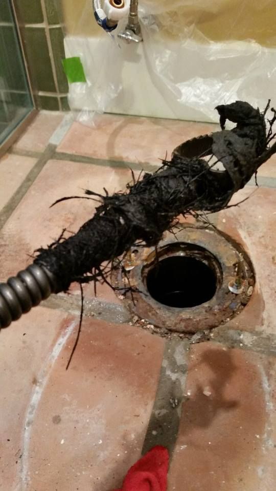 Drain unclogged: black hair and debris pulled from drainpipe on tiled floor with plumber's snake.