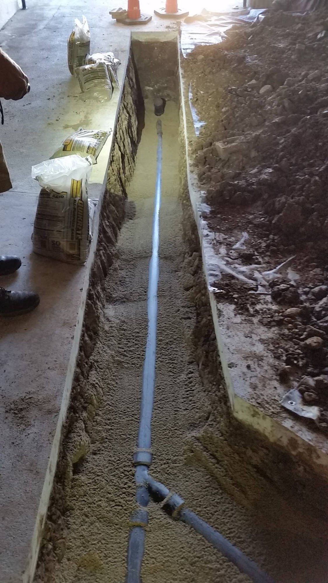 A trench dug in concrete floor with gray pipe running through it, construction site.