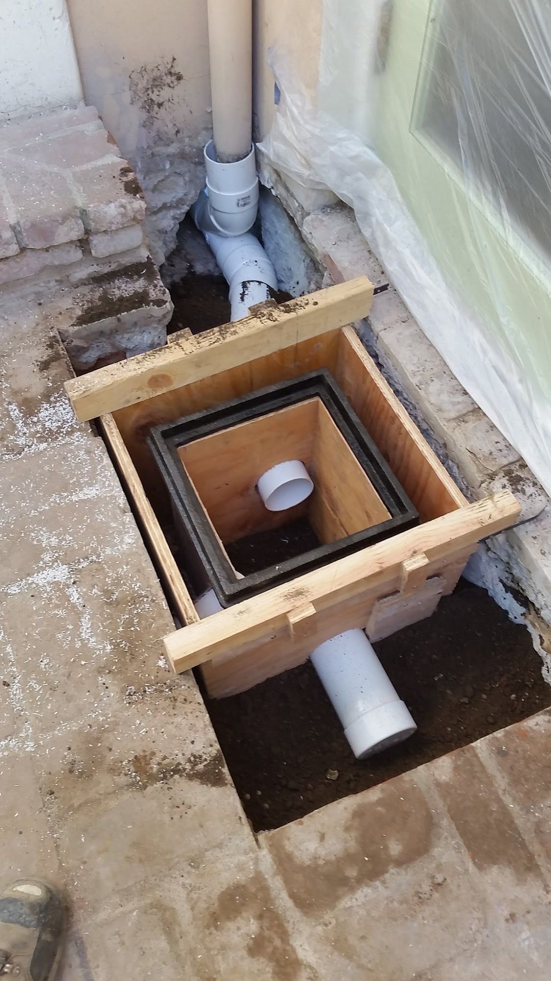 Drainage system installation with a square drain, piping, and wooden frame in progress outdoors.
