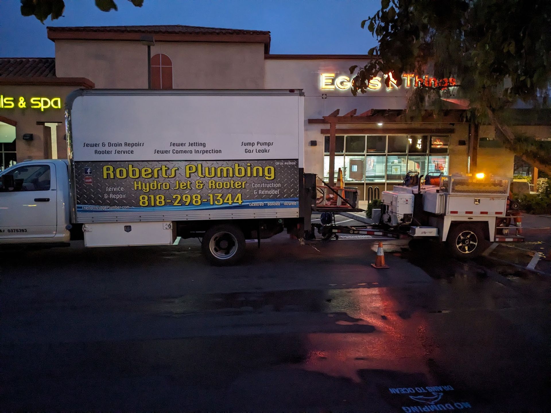 Roberts Plumbing truck parked outside a shopping center at dusk, with equipment attached and illuminated.