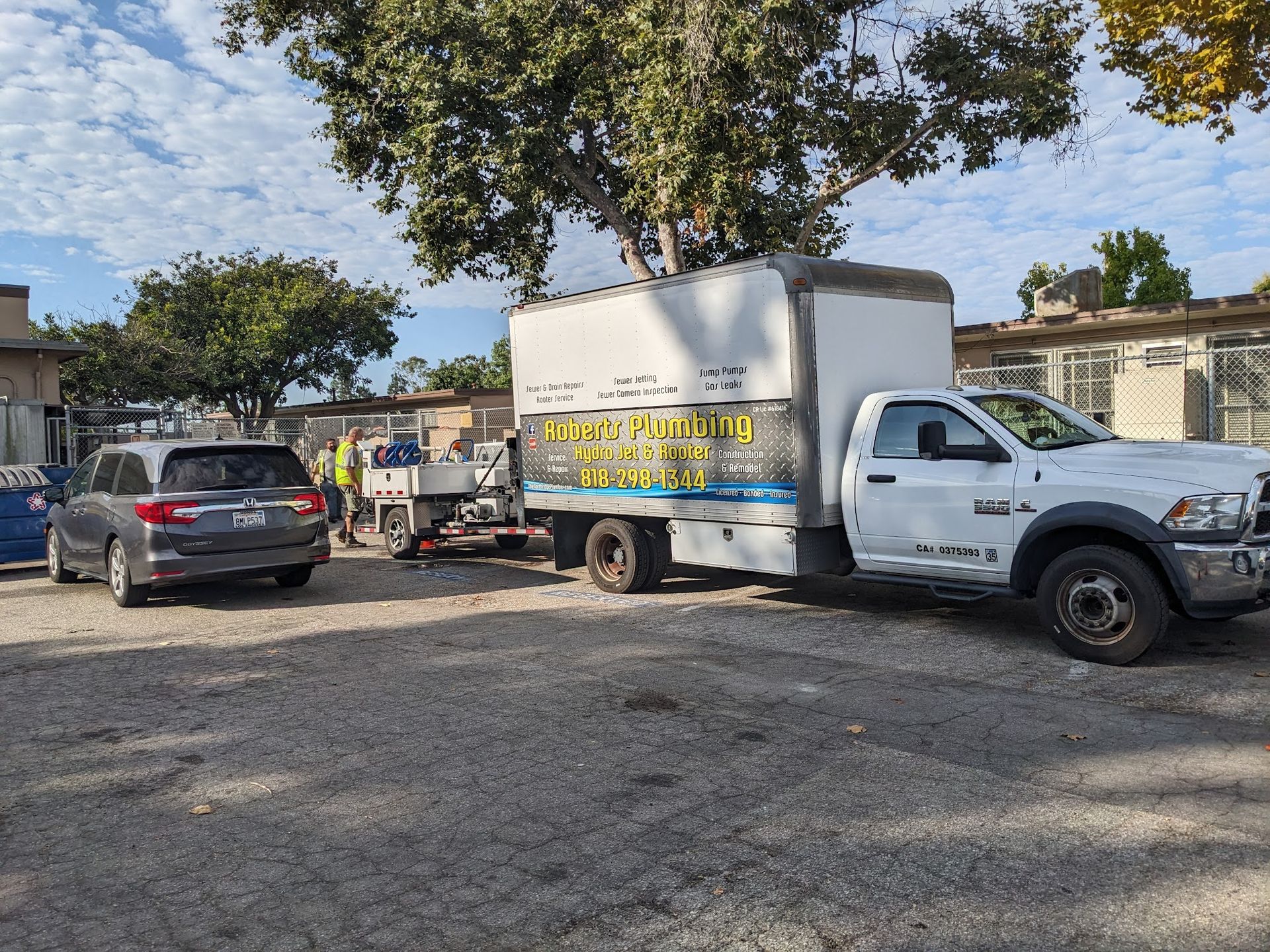 White truck with a box trailer parked on gravel, near a car and building.