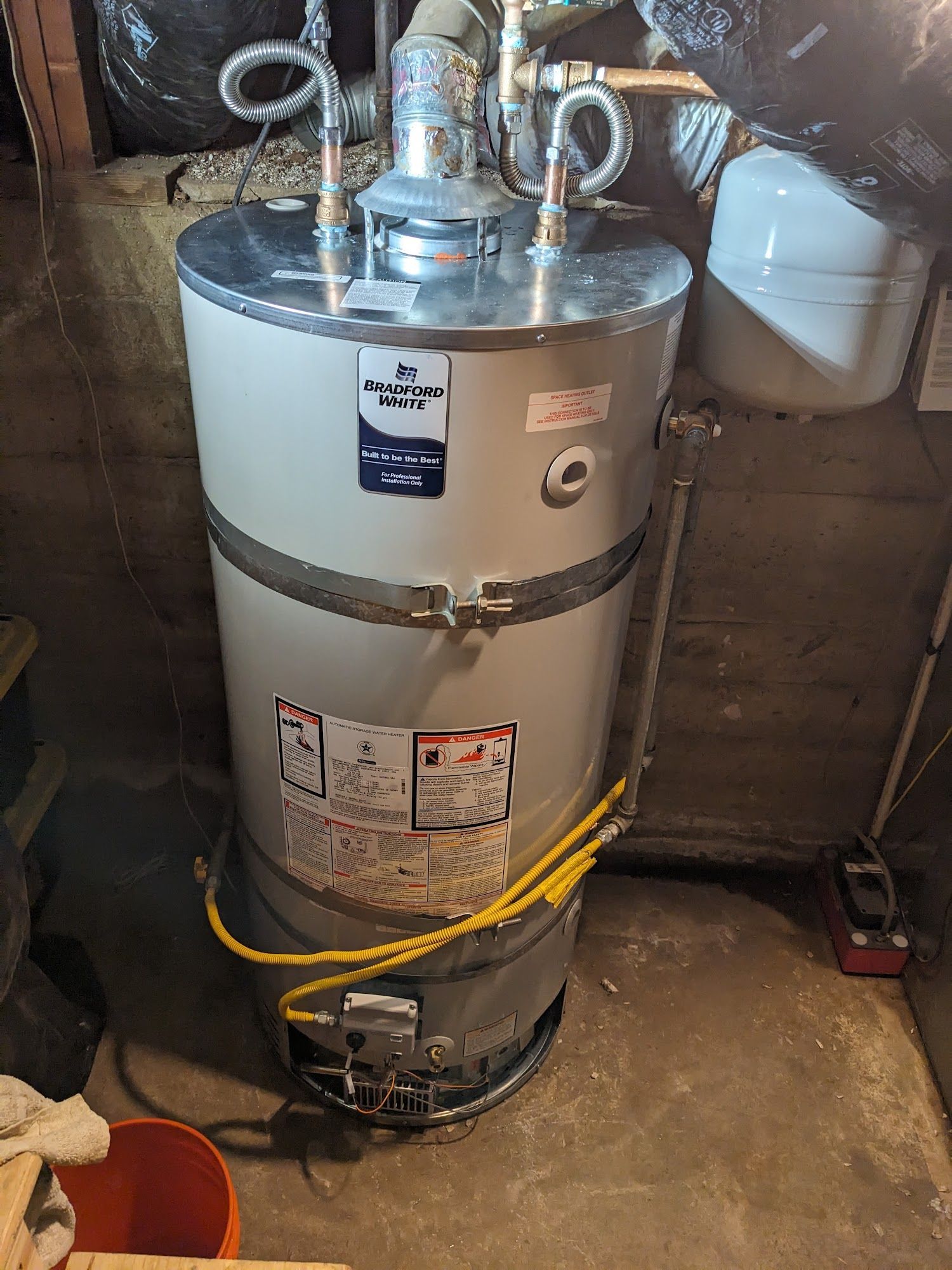 A gas water heater in a basement. The water heater is gray and silver, with yellow gas line.