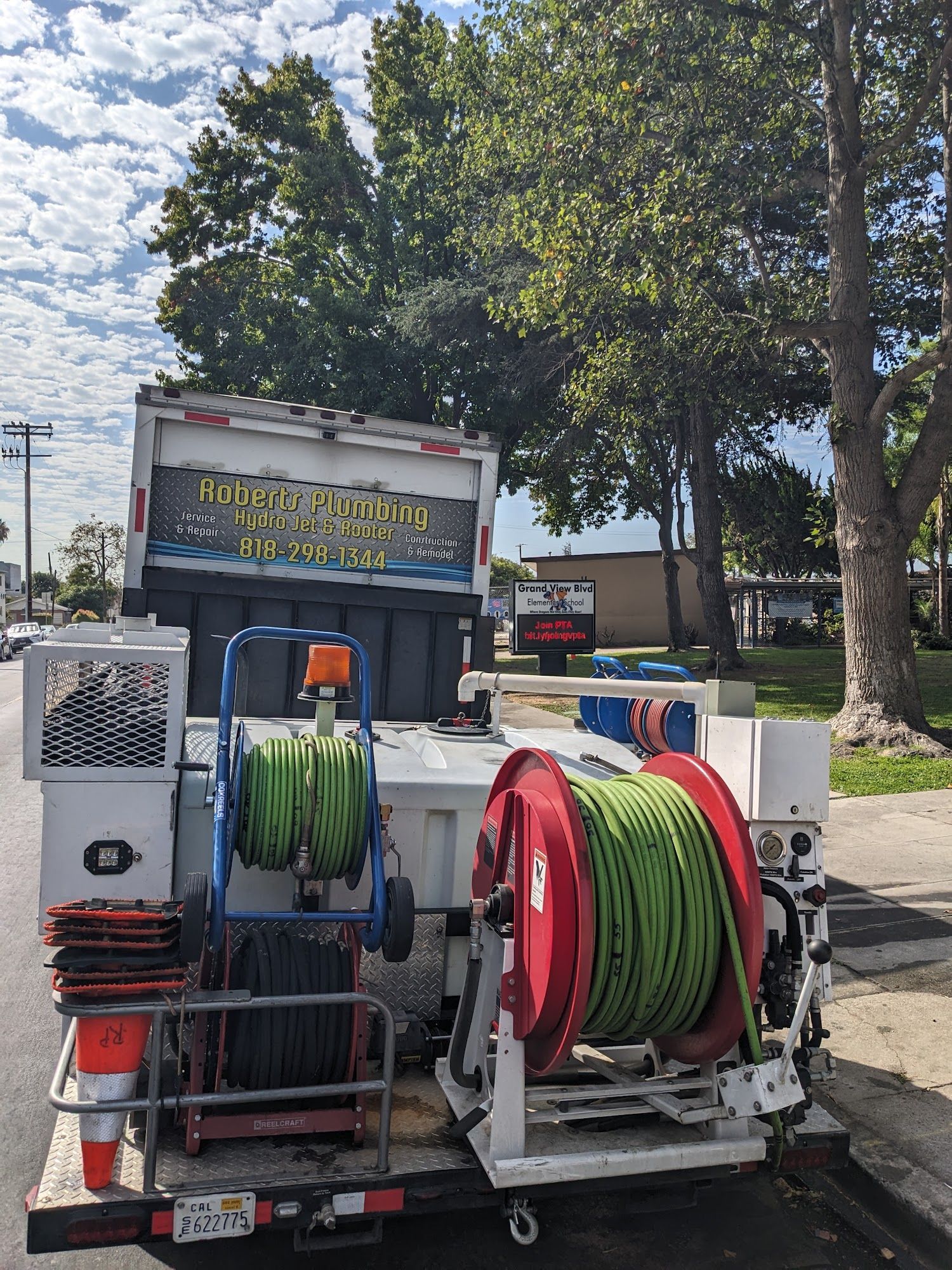 A white service truck parked on a street has green hoses and equipment. The truck’s sign is visible.