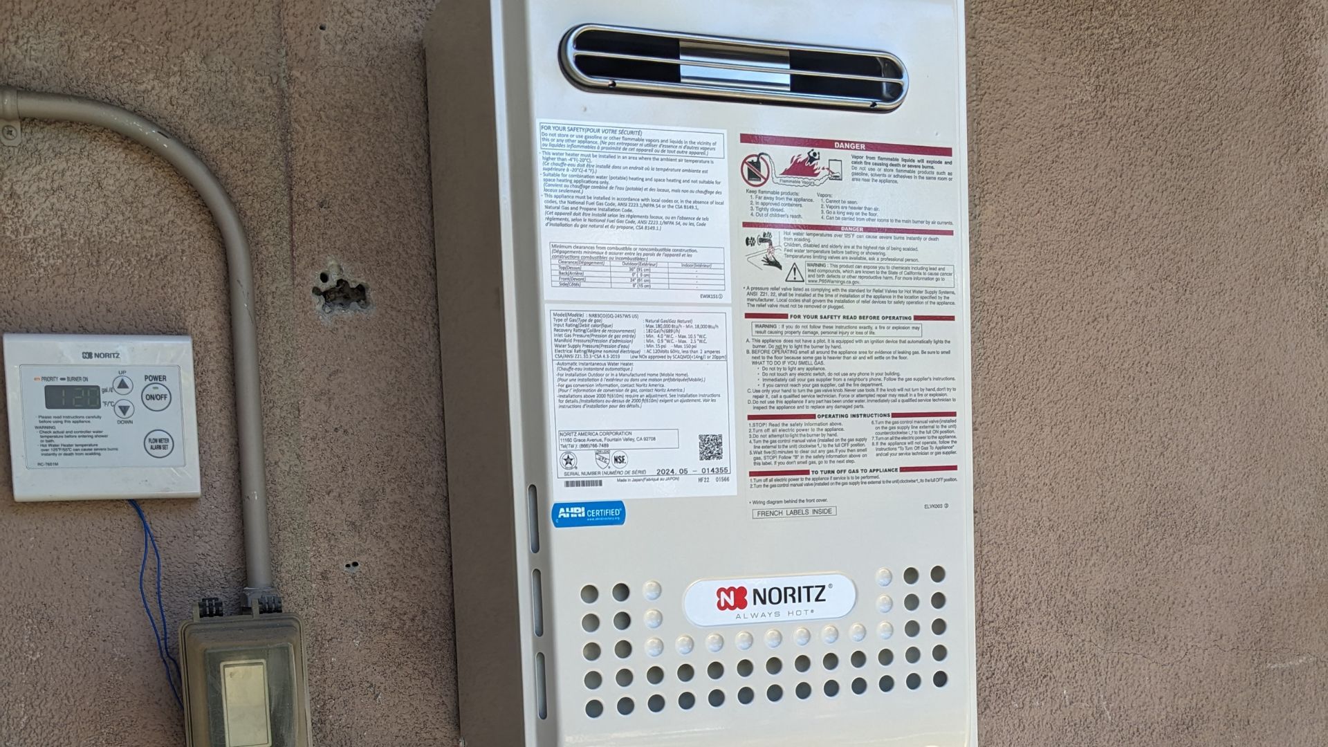 Outdoor tankless water heater mounted on a stucco wall, with a control panel and pipe.