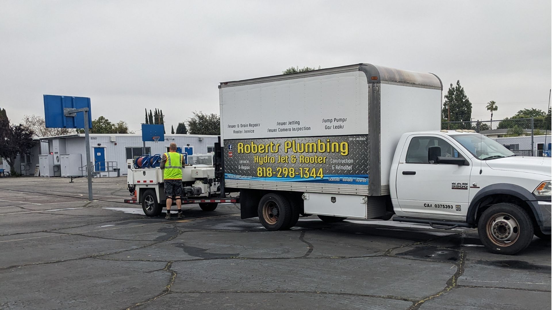 White truck towing a trailer, parked in a parking lot. A person is near the trailer. Buildings in the background.