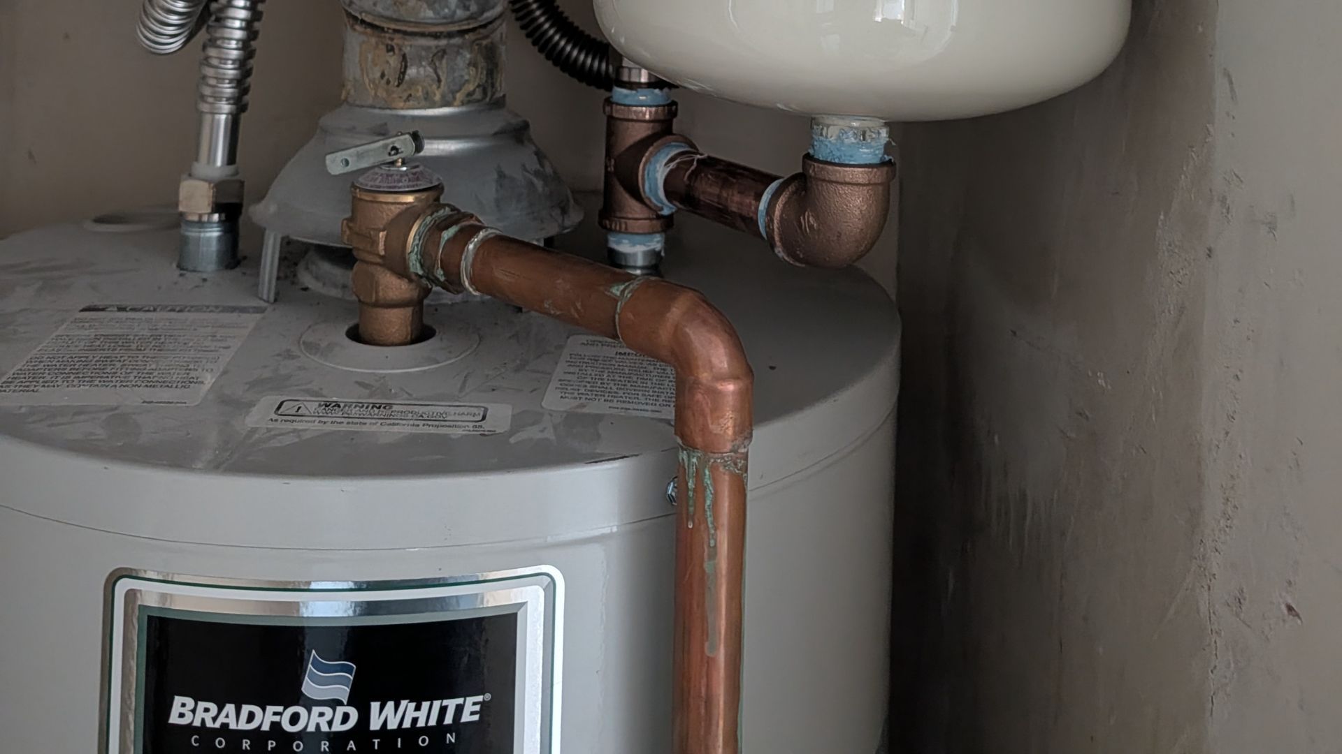 A water heater with copper pipes and a white expansion tank.