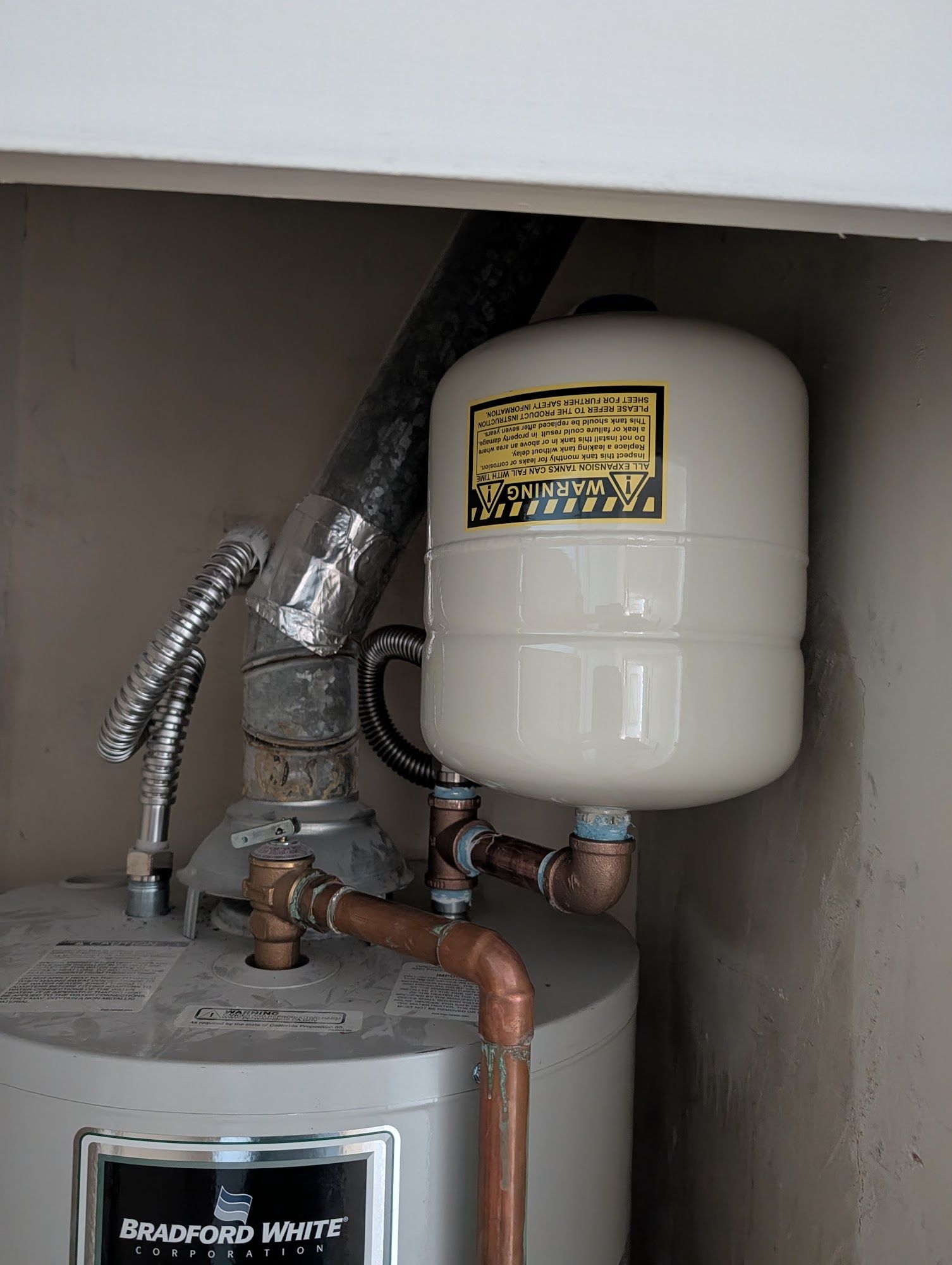 A water heater with an expansion tank, pipes, and venting in an enclosed space.