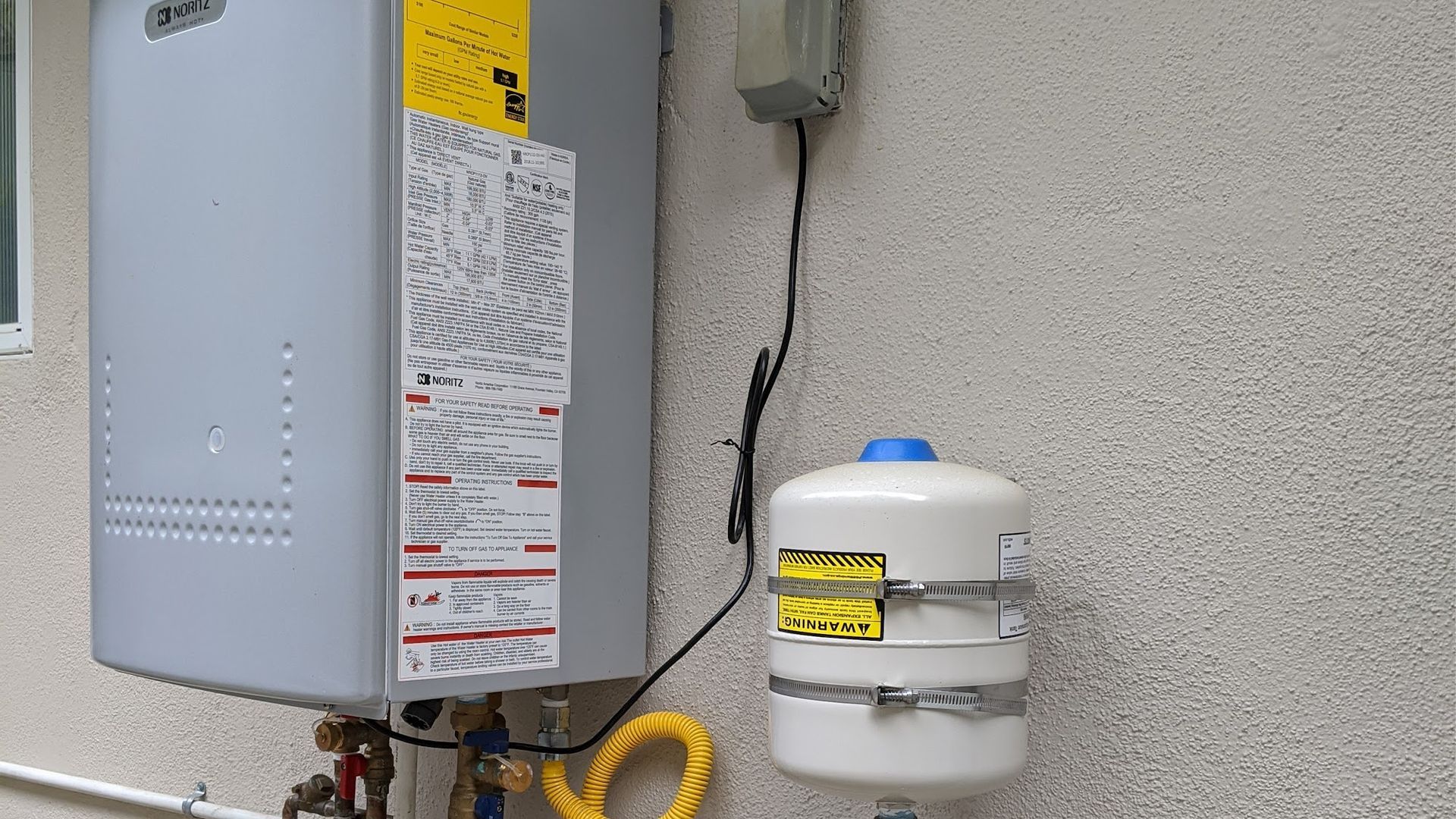 Gas water heater with expansion tank mounted on a textured exterior wall.