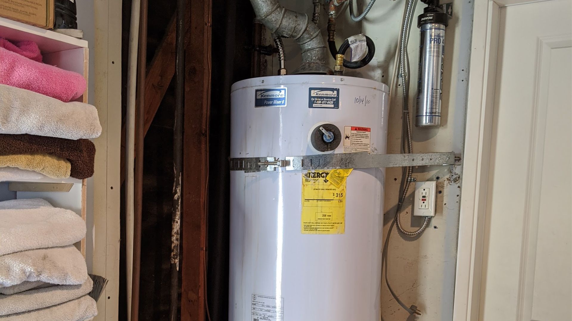 White water heater in a utility closet with towels on shelves to the left.