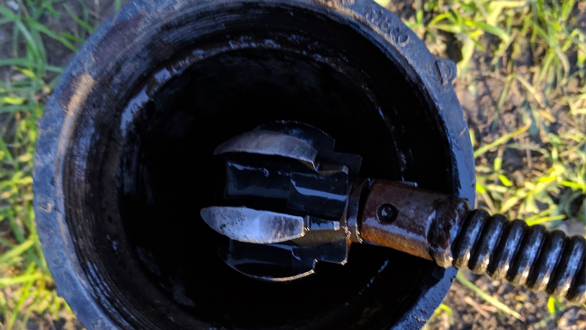 A plumbing snake with a cutter head inside a dark, open pipe.