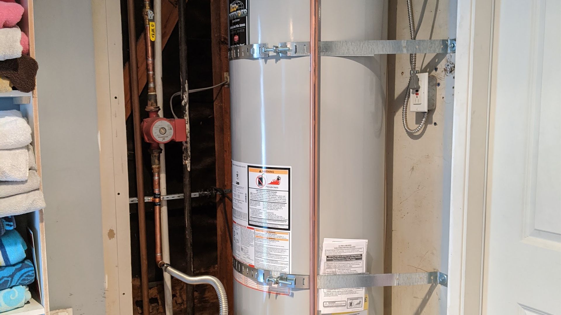 Water heater in a utility closet with copper piping and support brackets.