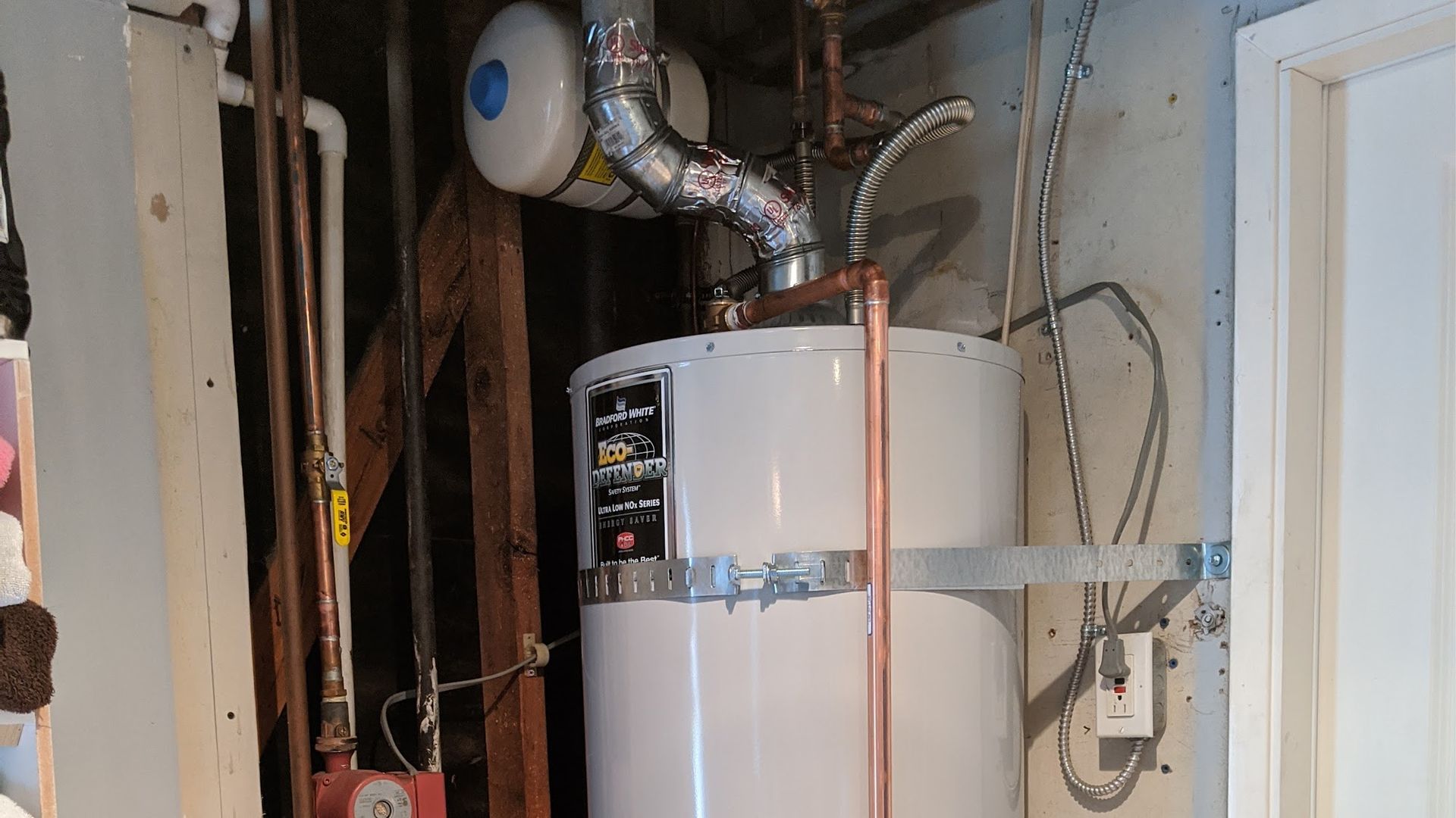 A hot water heater installed in a basement, with copper pipes and venting.