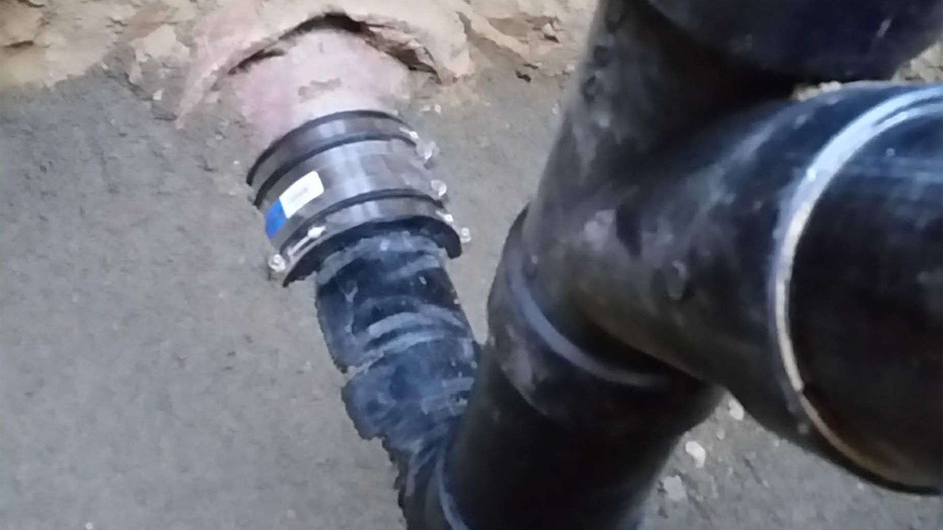 Black plumbing pipes connected underground with a coupling.