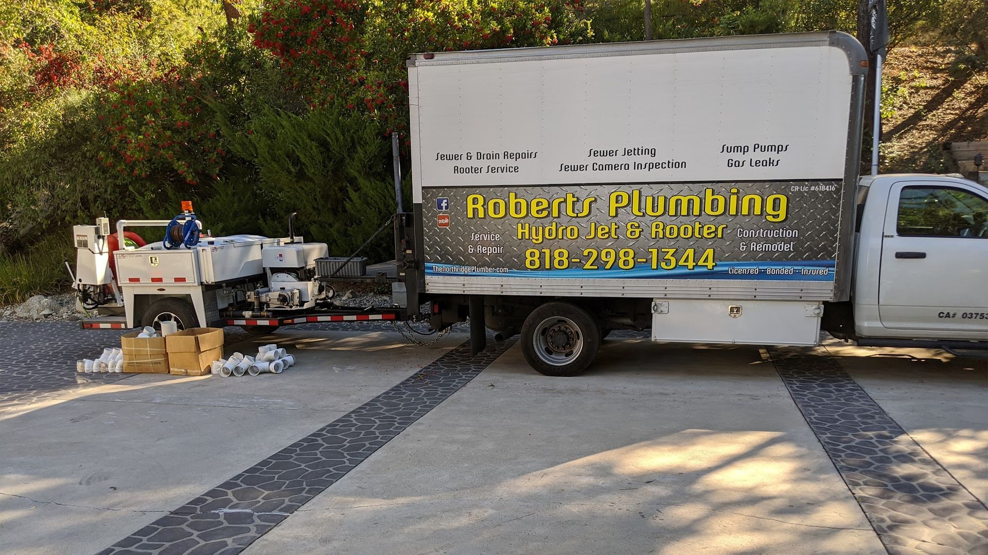 A white plumbing truck parked on a concrete surface with supplies and a trailer. 