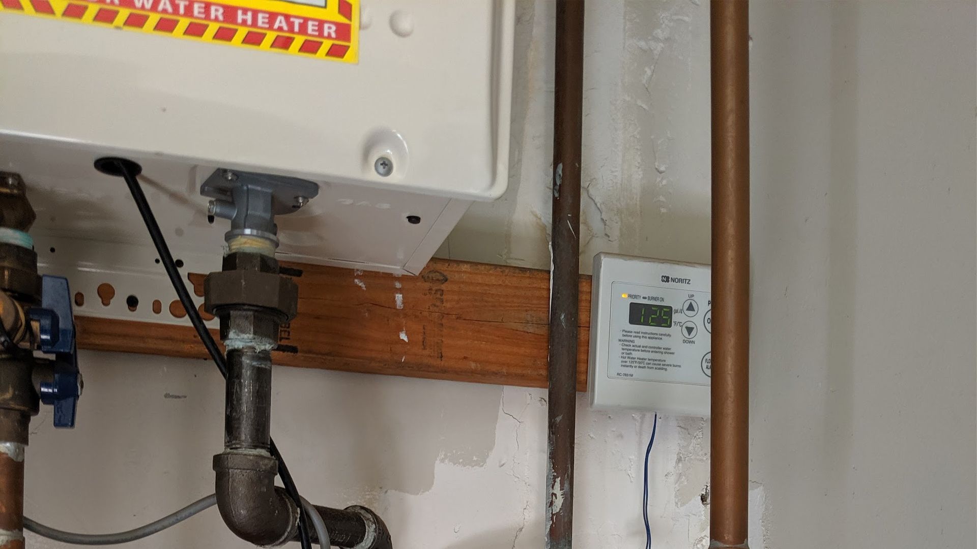 A water heater unit and thermostat on a wall with copper pipes.