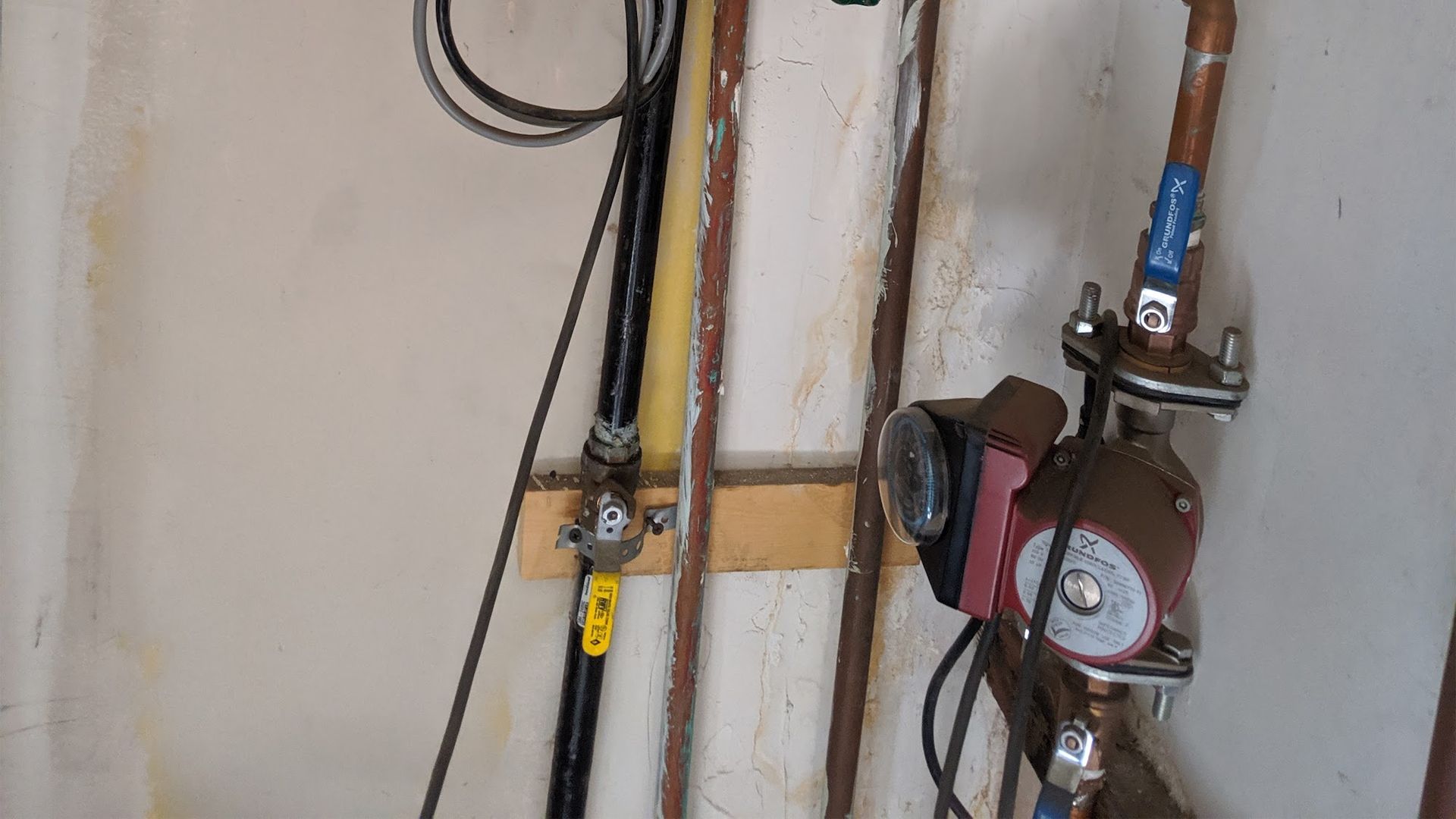 Pipes, a pump, and a valve mounted on a wall. Electrical wiring is visible.