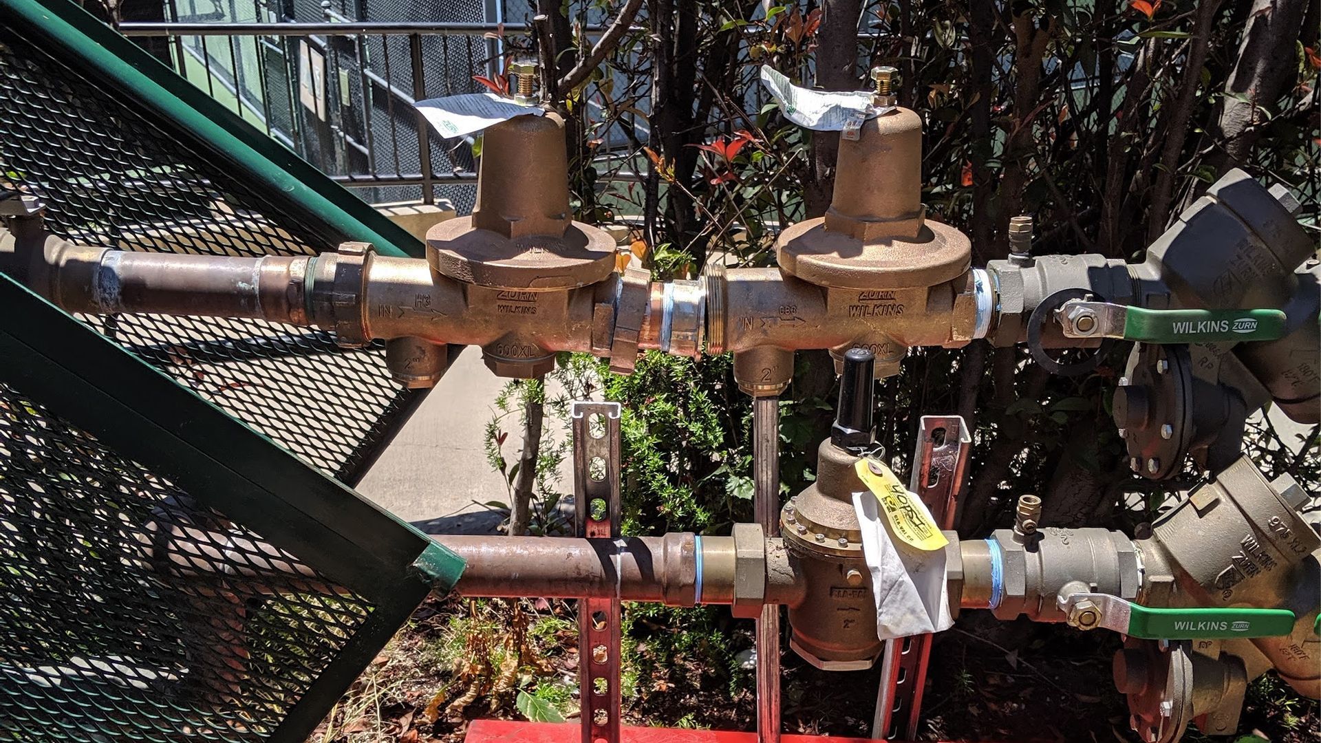 Plumbing pipes and valves outdoors, including pressure regulators and ball valves.