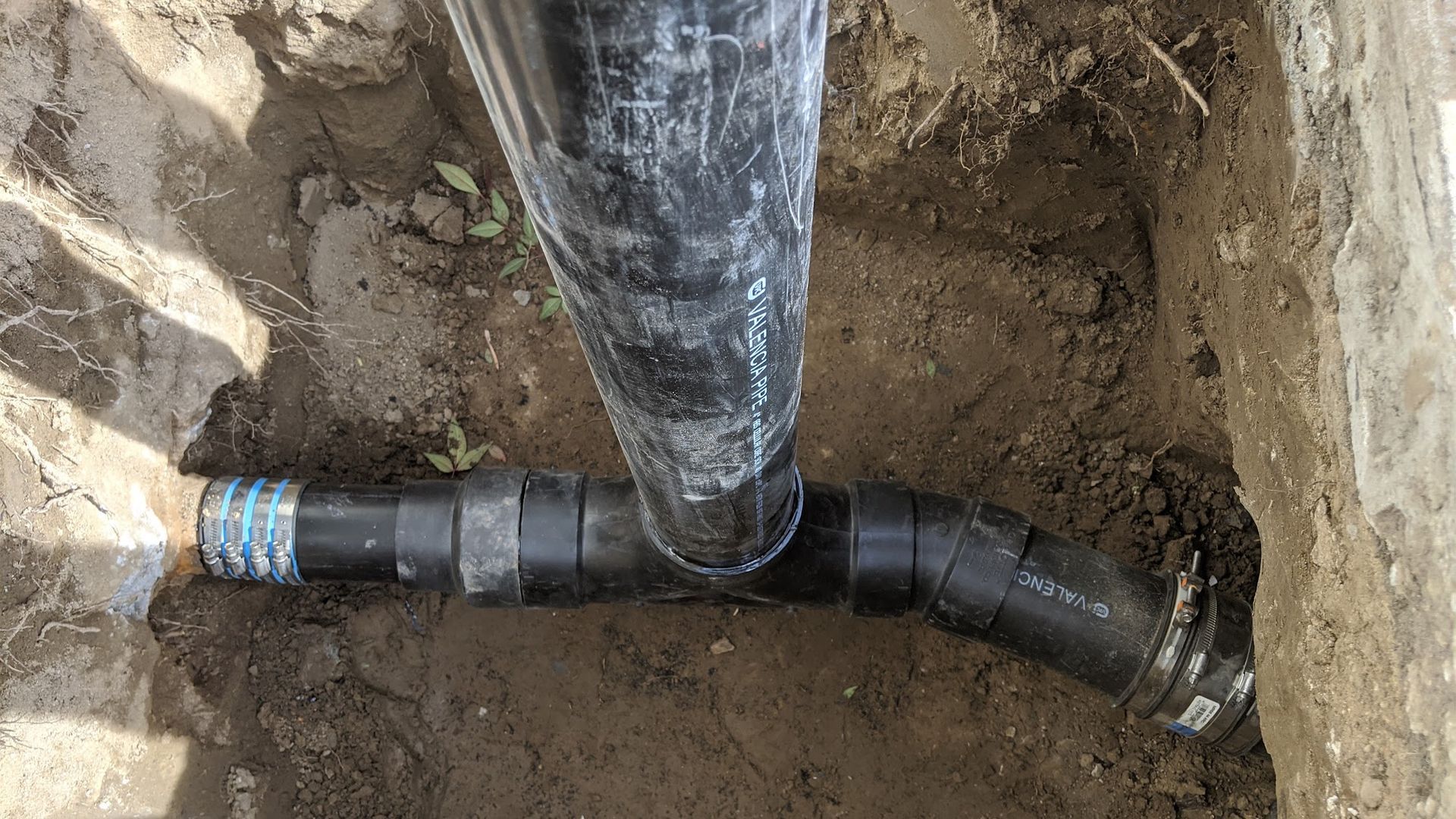 Black plumbing pipes in a dirt trench, connected with joints and bends.