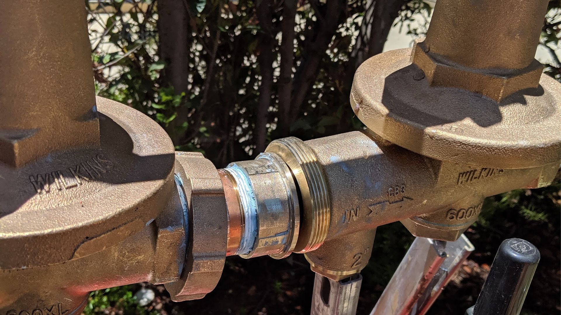 Brass plumbing components with copper pipe and connections outdoors.