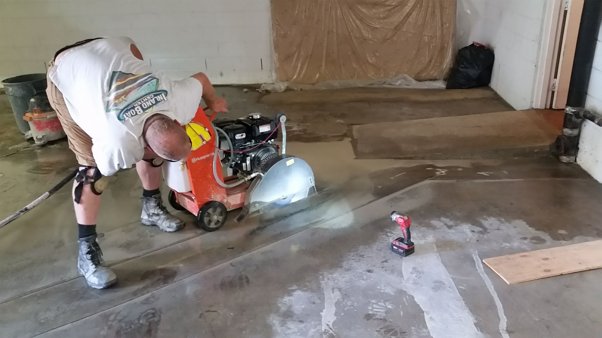 Person grinding a concrete floor with a machine. Drill and wood plank on the floor in a garage.