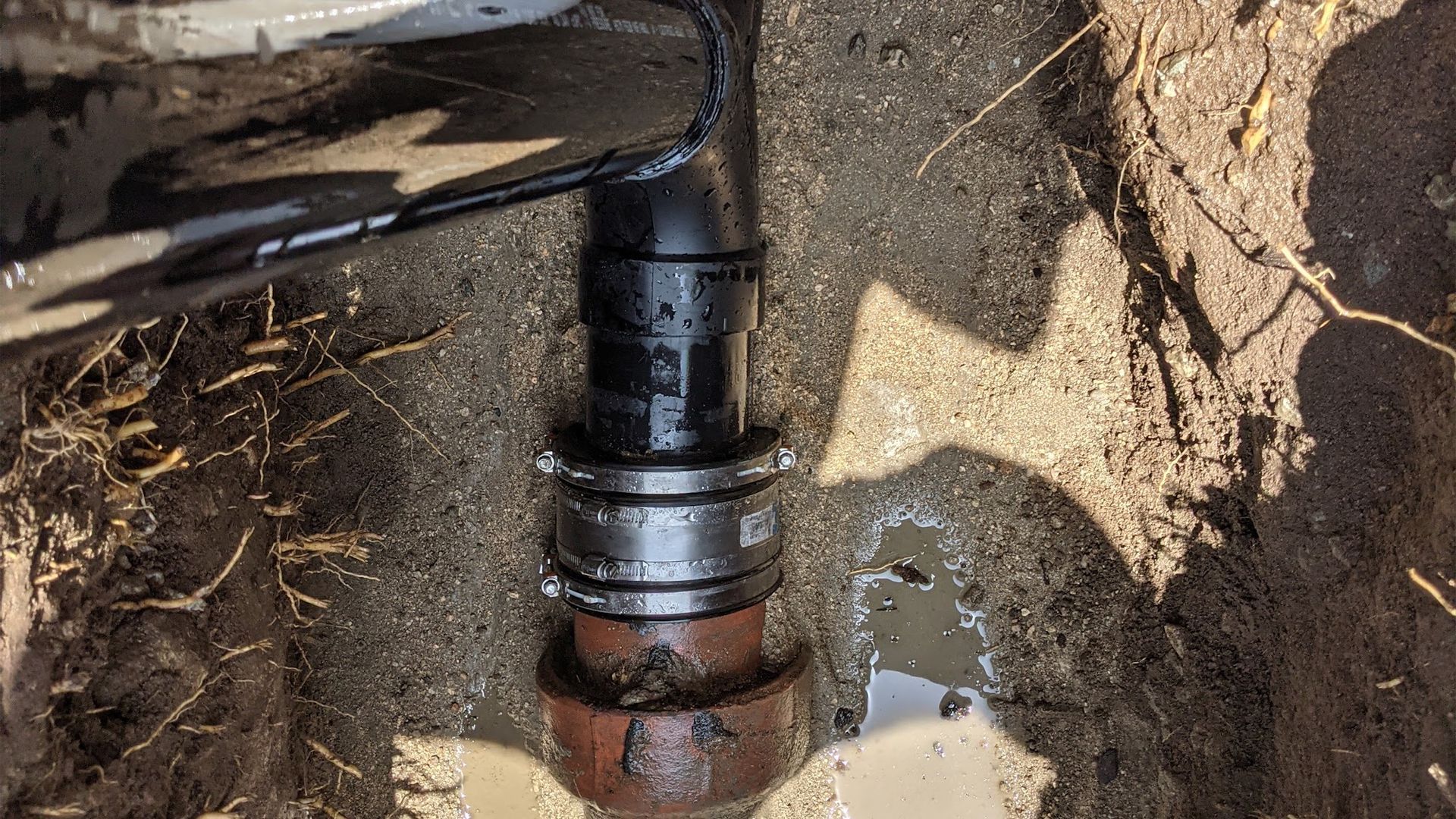 Black pipe fitting connection in a dirt trench, with water present.