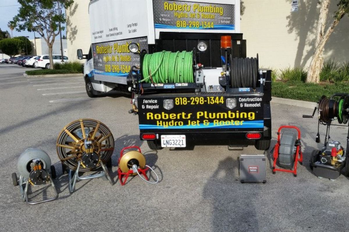 Plumbing truck with equipment in a parking lot. Tools include cables and a hydro jet. 