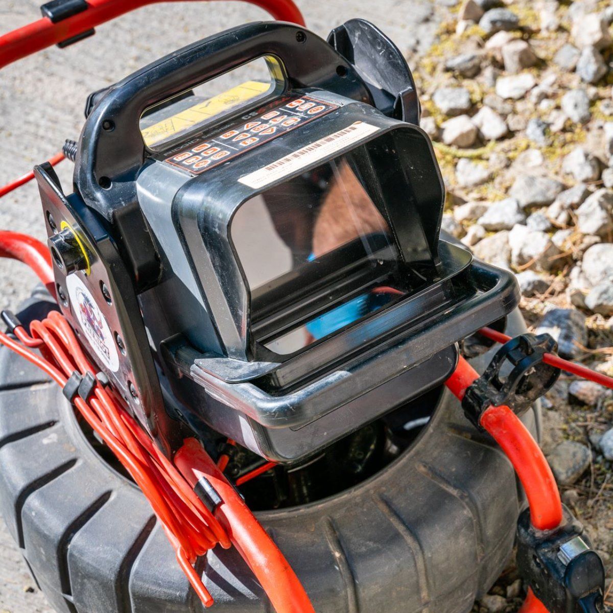 Black and red portable battery charger with handle and power cables on a tire.