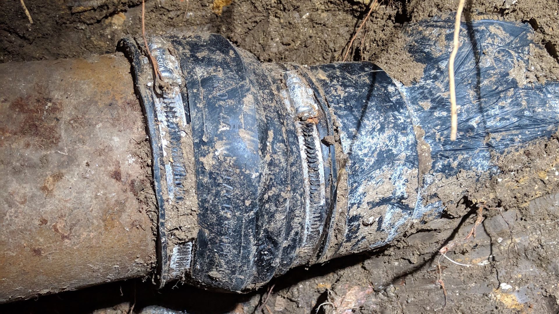 Black coupling joins two sections of buried pipe in dirt.