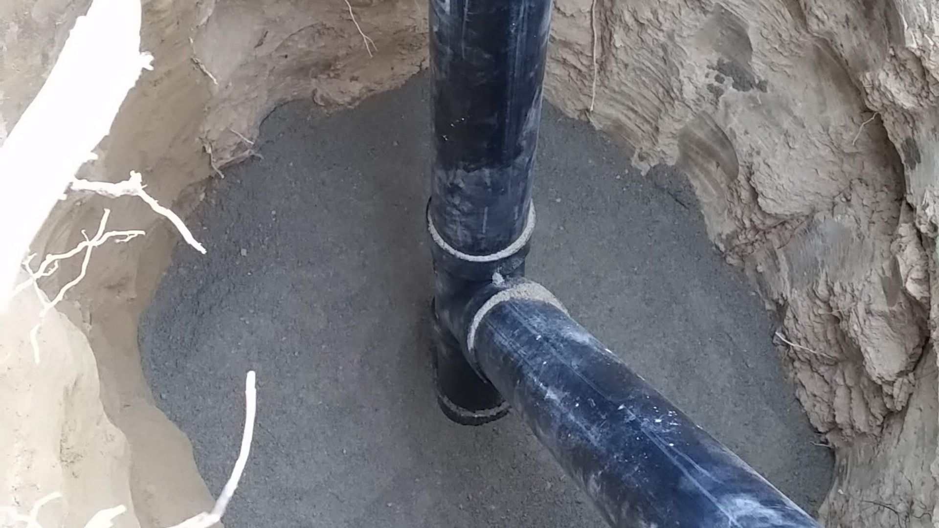 Black pipes joined underground in a gray cement-lined pit.