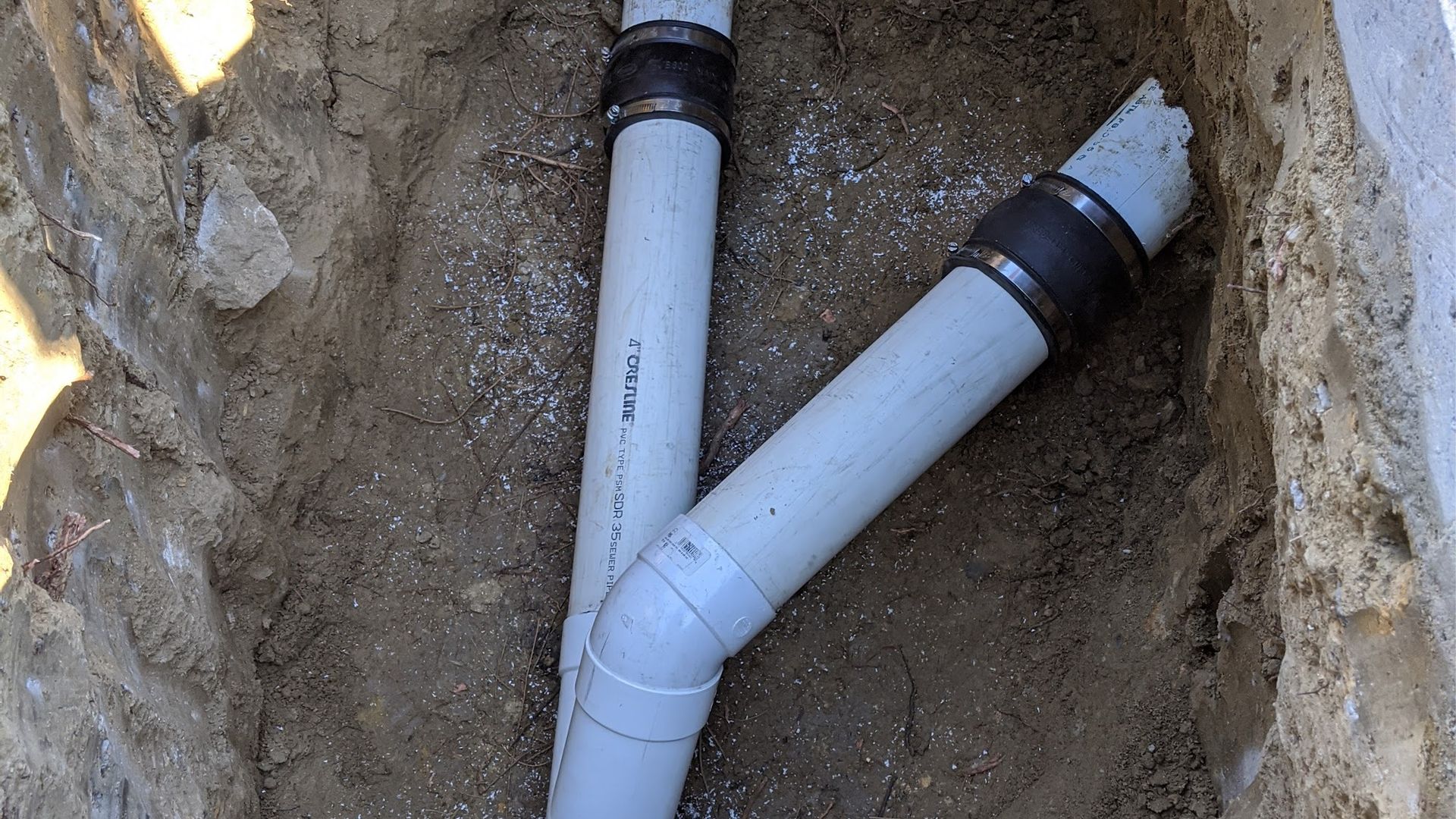 Two gray PVC pipes in a dirt trench, connected by a Y-fitting.