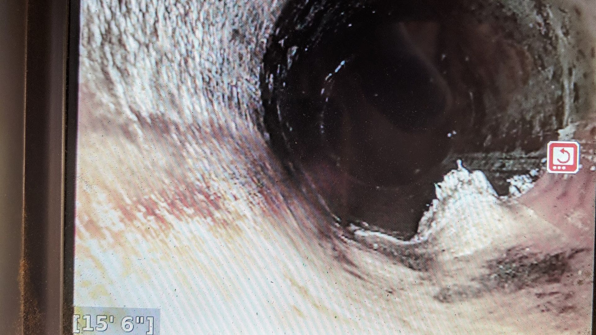 Inside view of a dark pipe with a large opening, appears to be a drain. The walls are discolored.