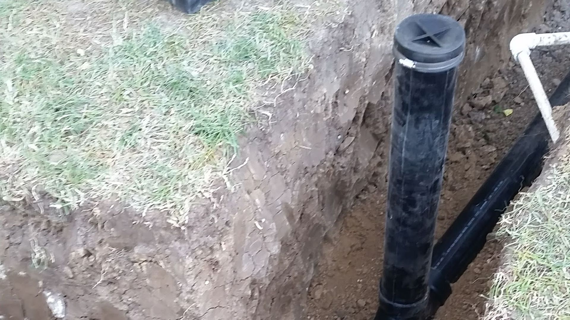 A black sprinkler system pipe in a trench next to grass.