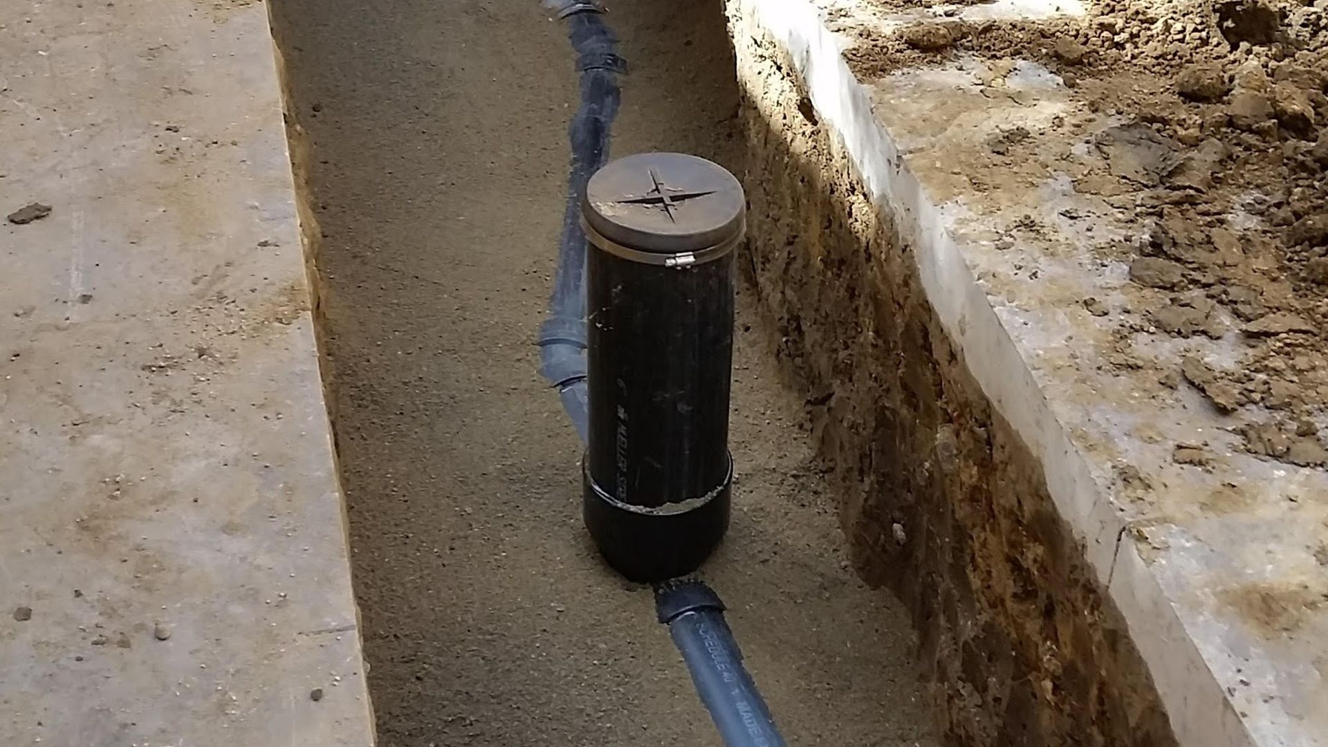 Black cylindrical object with a cap in a trench with pipes and dirt.