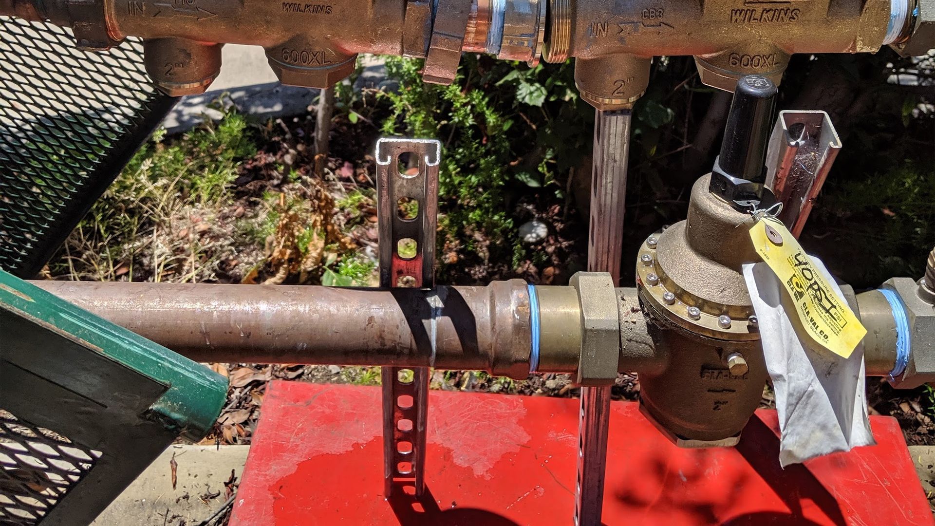 Copper pipes and a pressure regulator connected to a water supply, outdoors.