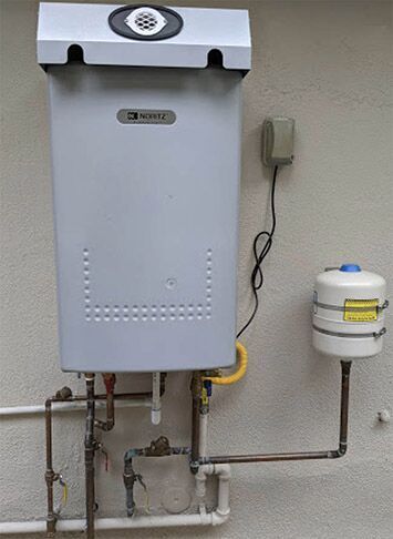 Tankless water heater and expansion tank mounted on an exterior wall with copper pipes.