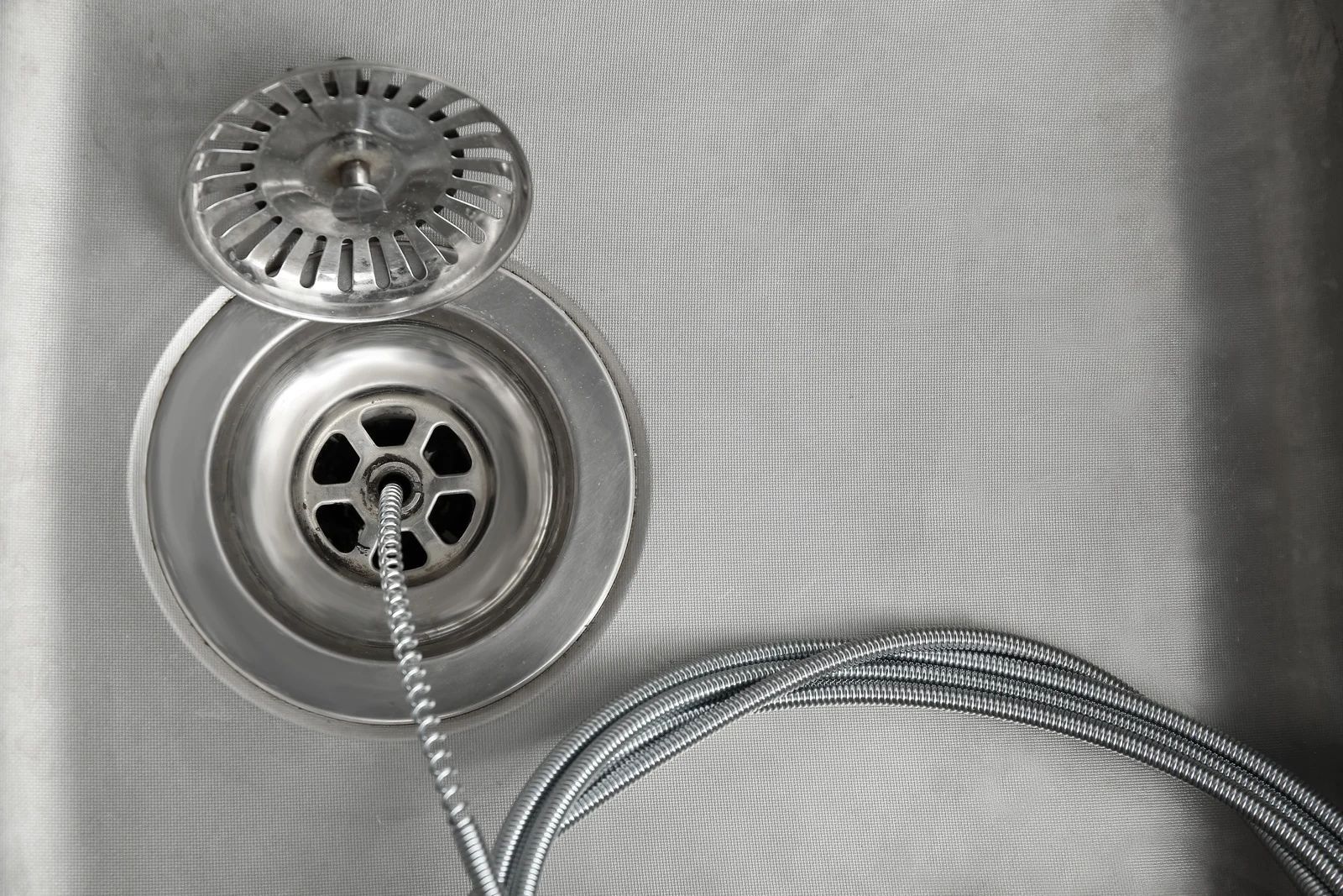 Chrome sink drain with stopper and braided hose on a textured white surface