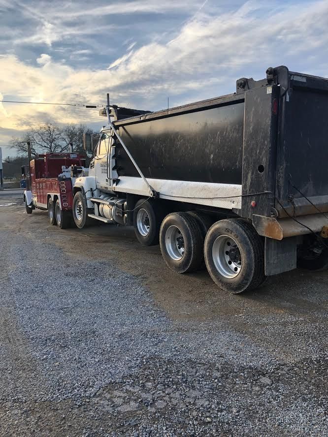 Dump truck on a gravel road, hauling a large load. The sky is partly cloudy.