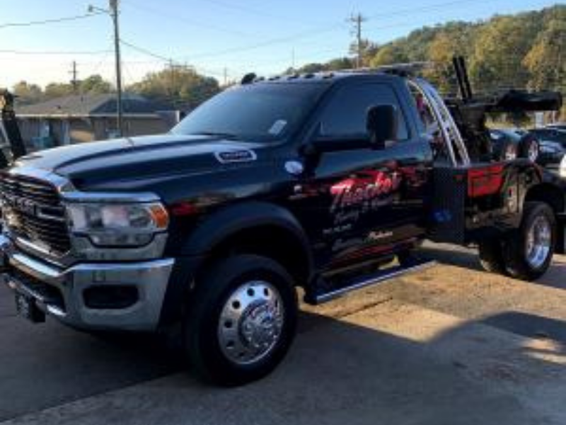 Black tow truck parked, with company name on the side, sunny day.