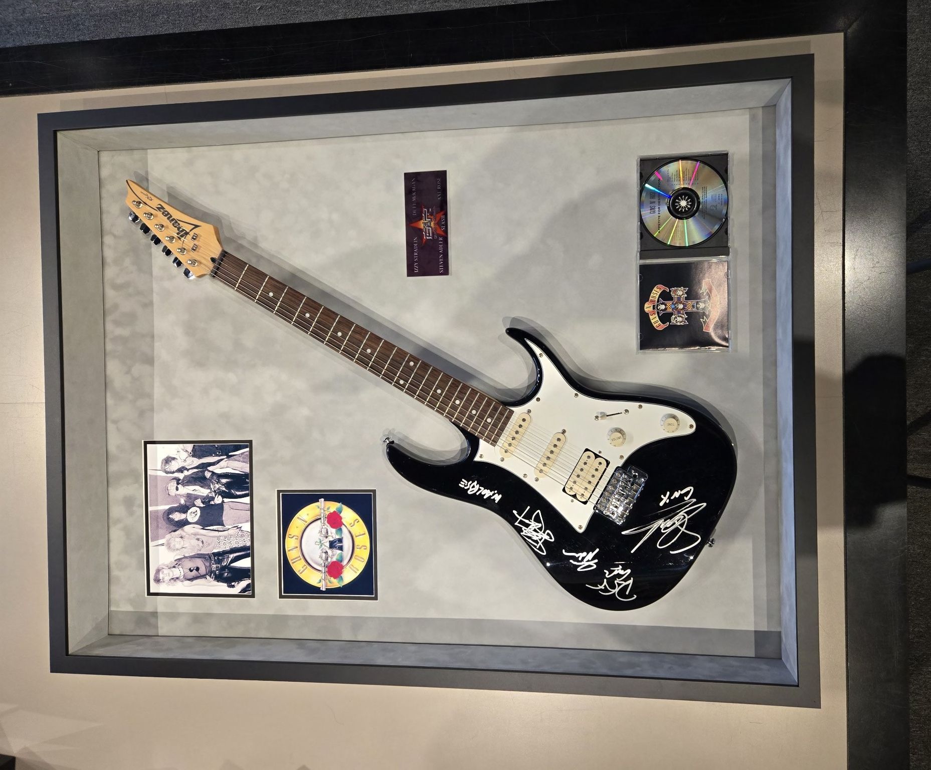 framed guitar with signatures and CDs surrounding it