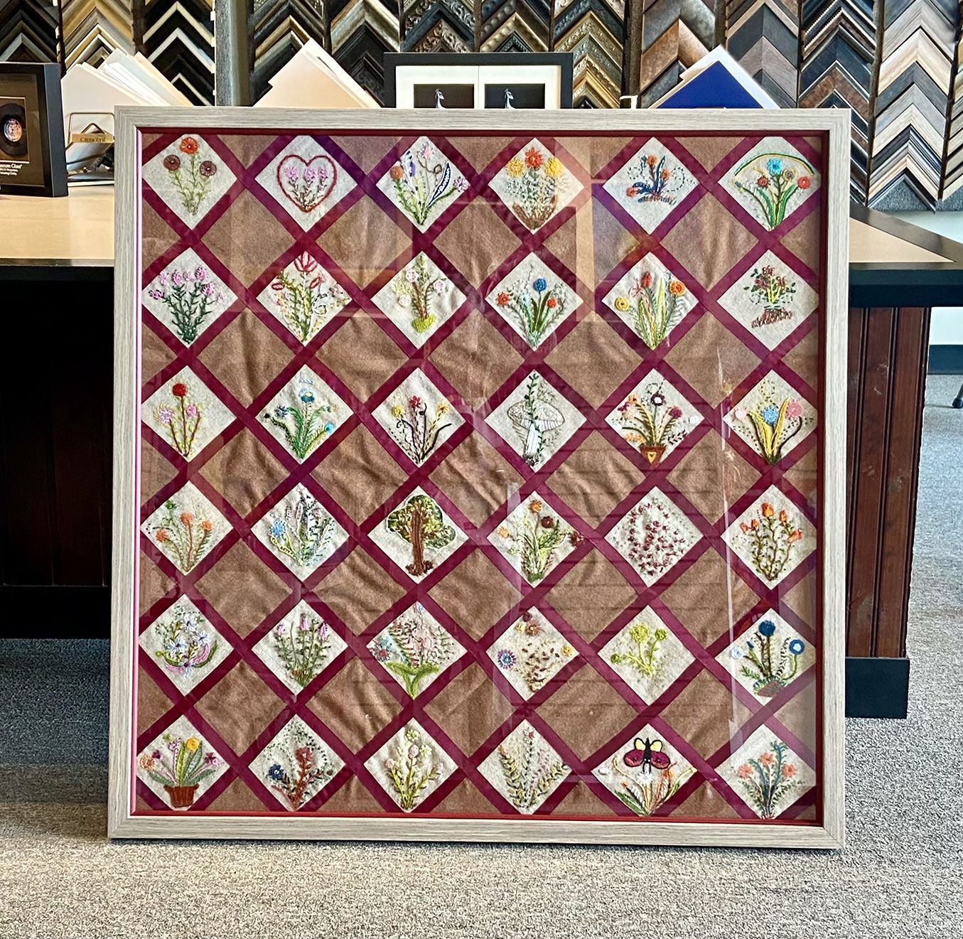 A framed quilt with flowers on it is sitting on a table.