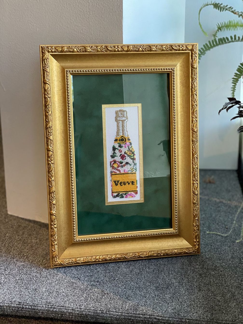A picture of a bottle of champagne in a gold frame.