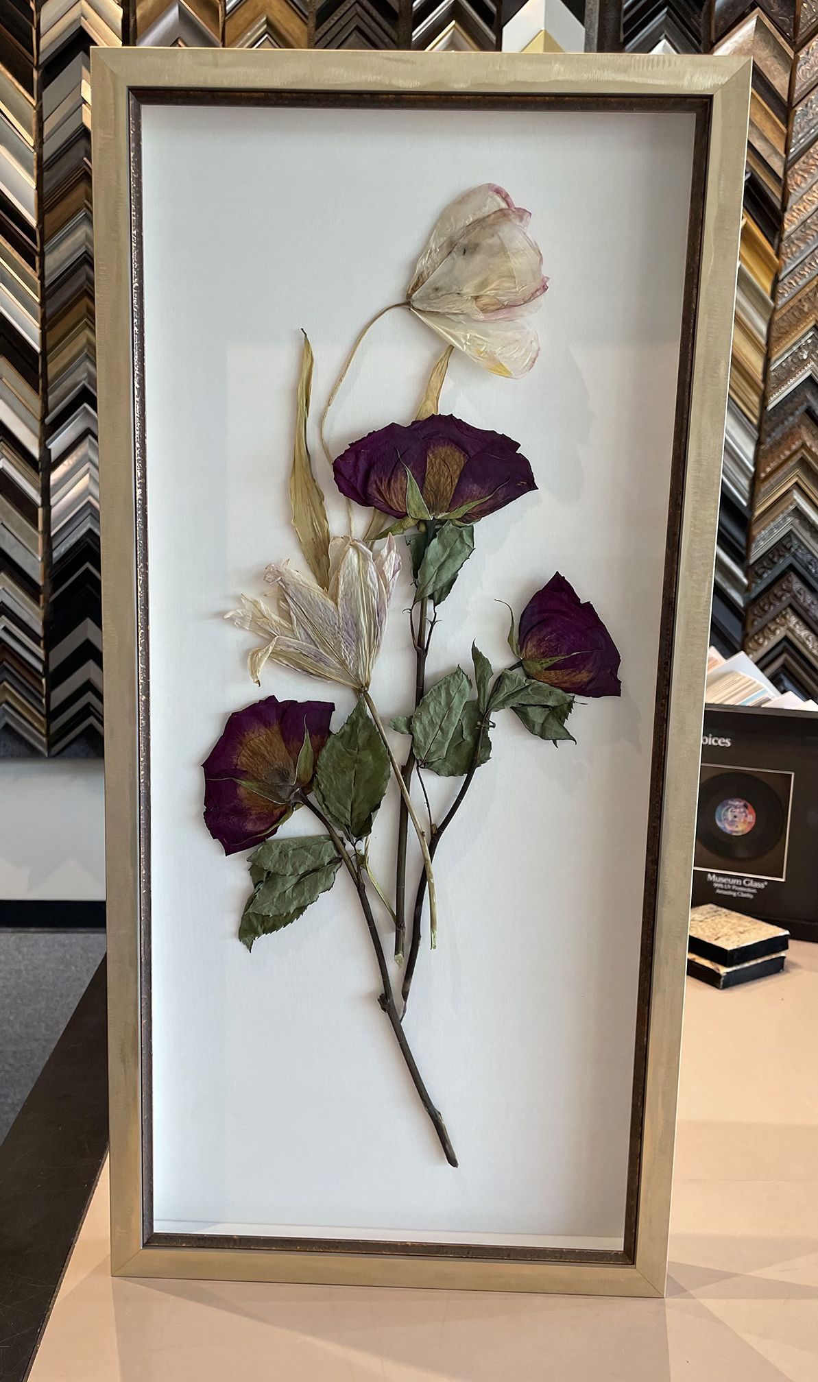 A picture of dried flowers in a frame on a table.