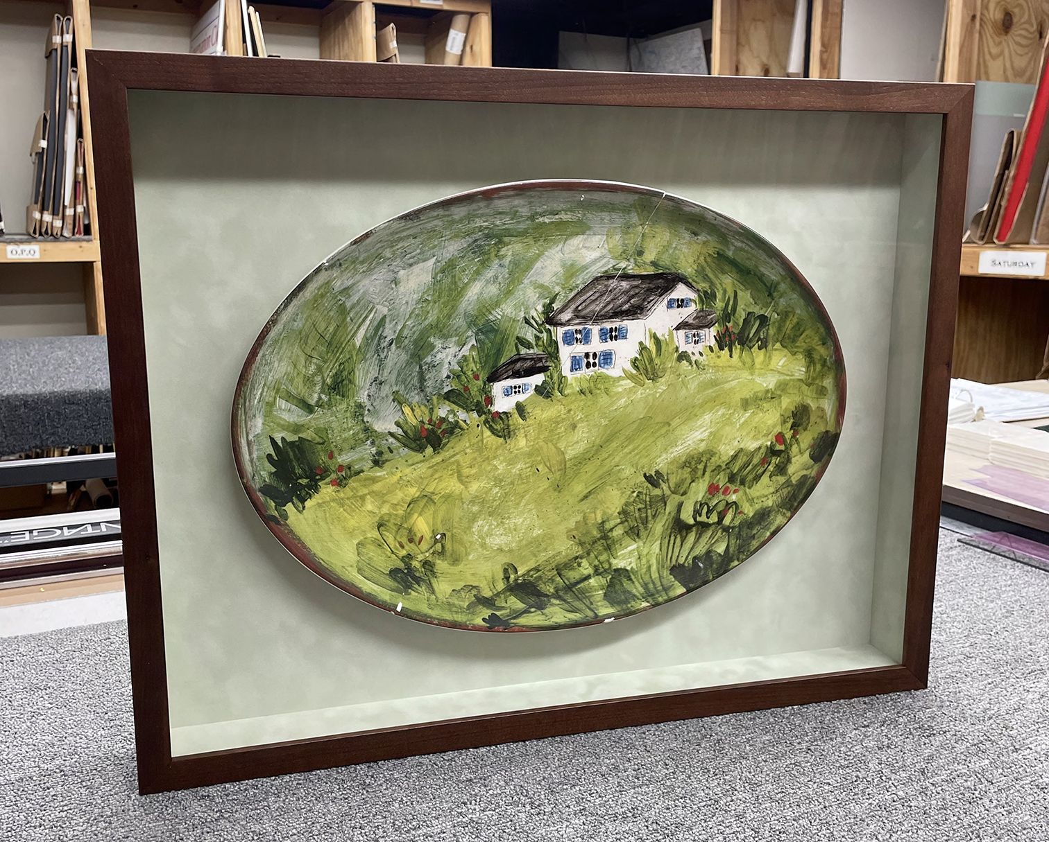 A painting of a house on a hill in a wooden frame