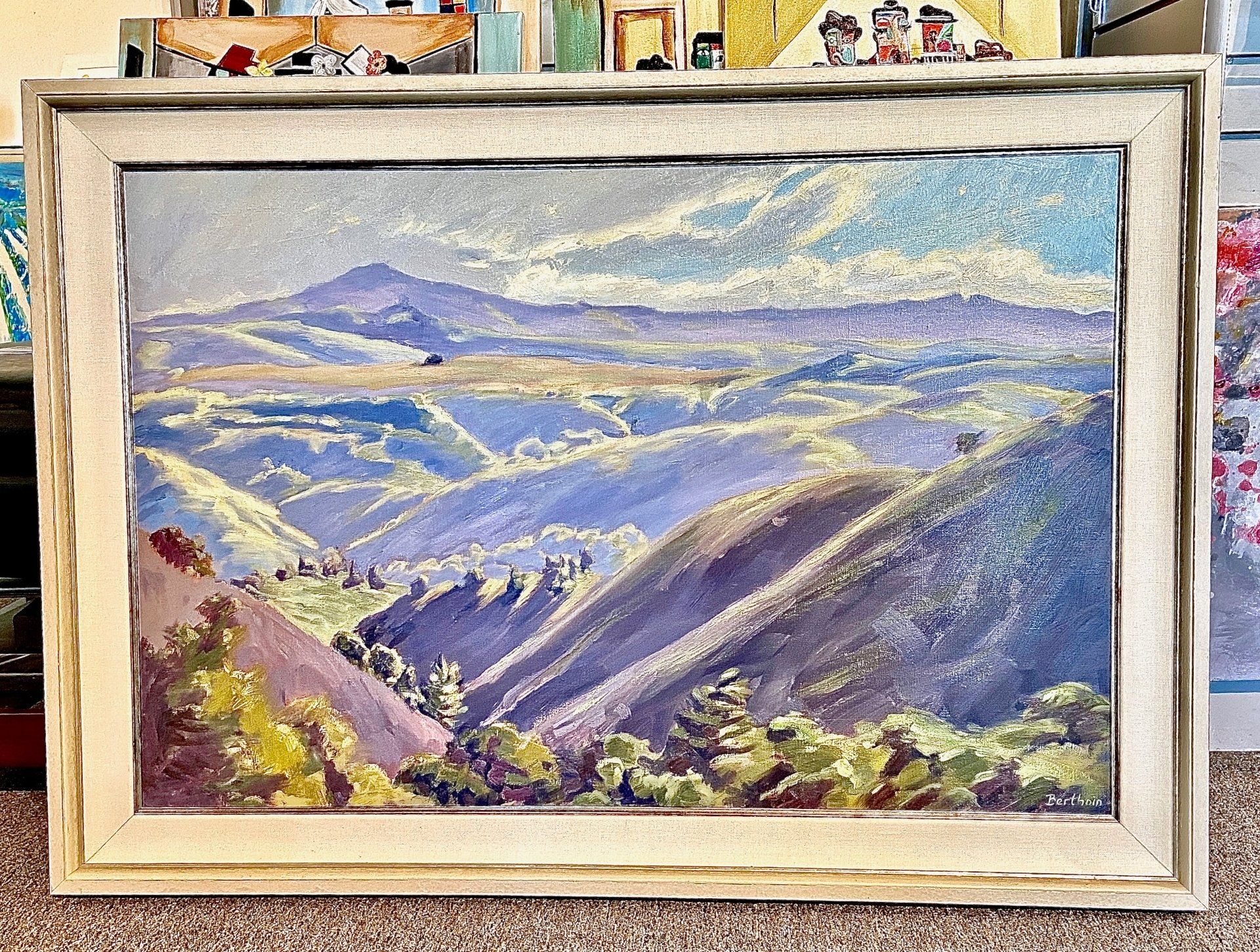 A framed painting of a landscape with mountains in the background