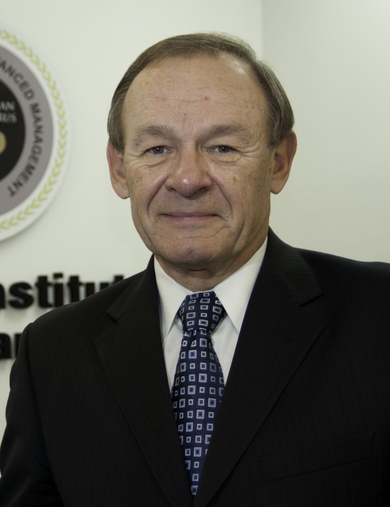 A man in a suit and tie stands in front of a sign that says advanced management