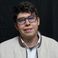 A young man wearing glasses and a jacket is smiling for the camera.