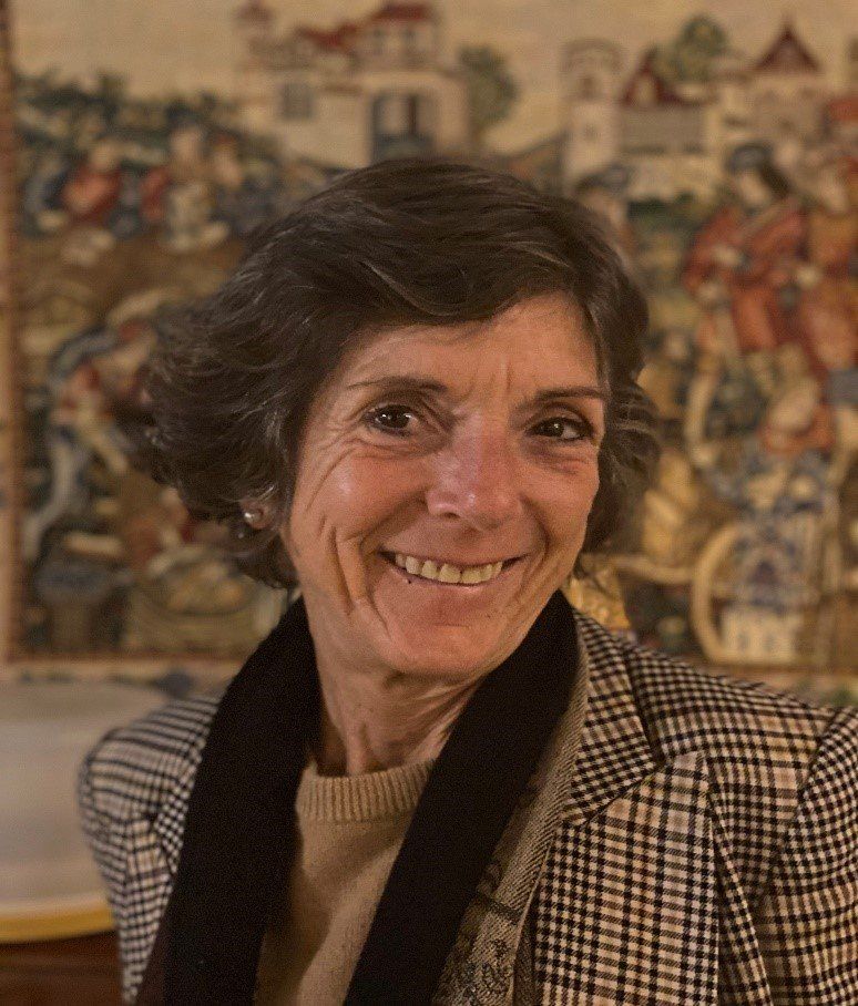 A woman in a plaid jacket and scarf is smiling in front of a painting.